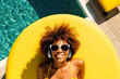 © ADDICTIVE STOCK - Top view of Generative AI illustration of happy African American female in sunglasses with Afro hair lying on inflatable yellow air mattress near swimming pool and listening to songs on headphones