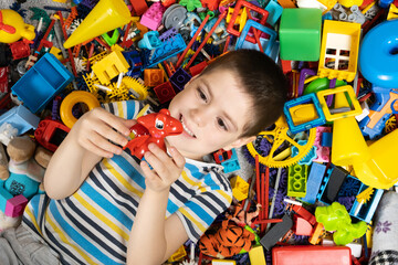 Cute little boy playing with toys lying among colorful toys on the floor, top view