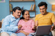 © WESTOCK - Happy Indian adult son with senior parents discussing from laptop while sitting on sofa at home - concept of property selection, online shopping and Family bonding.