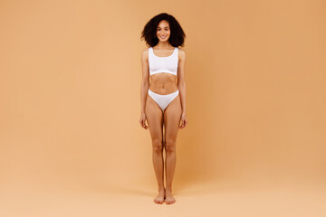 Wall Mural - Full length portrait of young black slender lady with perfect body shape and flat tummy posing on beige background