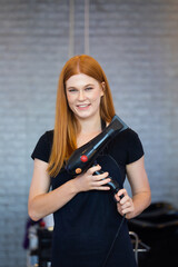 Wall Mural - Young caucasian female professional hairdresser holding hair dryer tools in beauty salon