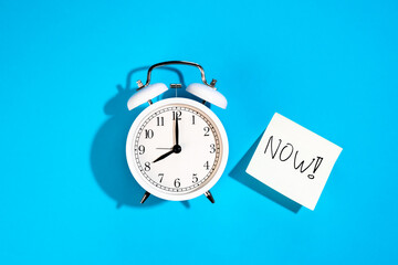 White alarm clock and a sticker with the inscription Now on a blue background.