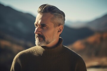 Sticker - Portrait of a handsome mature man with grey hair and beard in a sweater on a background of mountains