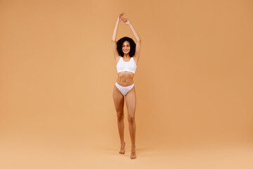 Wall Mural - Sensual black woman posing in white underwear, raising hands up, showing beautiful curves of her body, full length