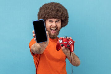 Wall Mural - portrait of excited man with afro hairstyle wearing orange t-shirt holding out showing joypad and sh