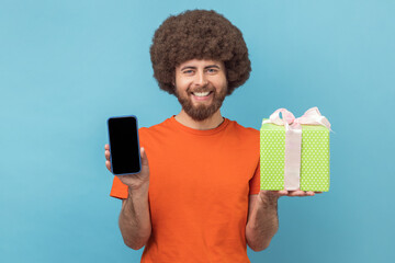 Wall Mural - portrait of satisfied man with afro hairstyle wearing orange t-shirt standing with present box and s