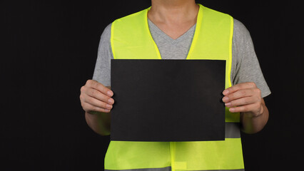 Wall Mural - Blank empty black paper in man hand and wear safety Vest on black background.