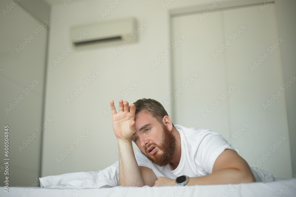 Man Using Ac Young bearded man using air conditioner at home, lay on bed cooling off ...