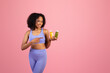 © Prostock-studio - Positive millennial black lady in sportswear hold jars of juice or smoothies isolated on pink background