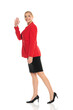 Middle aged senior smiling business woman in red jacket and black skirt walking on white background and wave hand. Side, profile view.