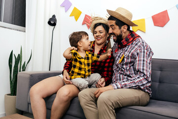 Brazilian Junina party at home. Family celebrating Festa Junina in the living room, wearing typical clothes and the wall decorated with colorful flags.