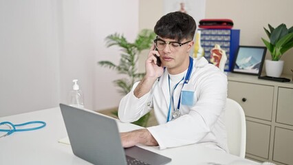 Canvas Print - Young hispanic man doctor using laptop talking on smartphone at clinic