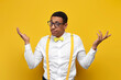 insecure guy african american in white shirt with suspenders and bow tie spreads his arms on yellow background