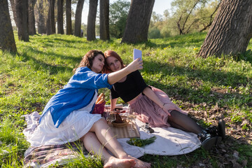 Two young and beautiful women taking a selfie outdoors on a picnic in nature