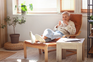 Canvas Print - Mature woman with cup of tea resting on armchair at home