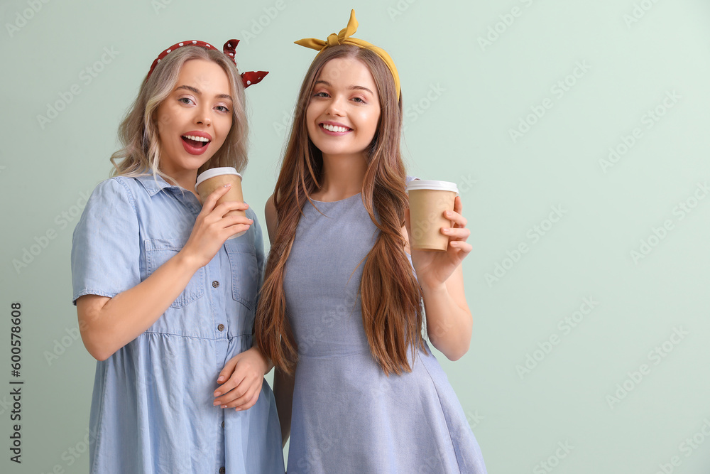 Young sisters with cups of coffee on green background