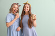 © Pixel-Shot - Young sisters with cups of coffee on green background