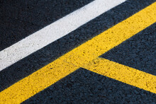 Road marking on brand new asphalt surface of a parking lot, yellow and white lines as abstract background