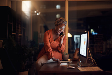 Wall Mural - Business, black woman and phone call on smartphone, computer typing and conversation at night. Happy worker, cellphone and communication for desktop management, mobile network and overtime in office