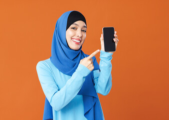 Beautiful overjoyed young smiling muslim woman in traditional religious hijab shows smartphone screen