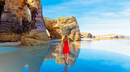 Beautiful woman with red dress walking in famous beach of cathedral- Travel in Spain, Galicia