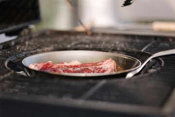 Wall Mural - Tasty beef steak is fried in a carbon steel pan that stands on hot coals. BBQ concept