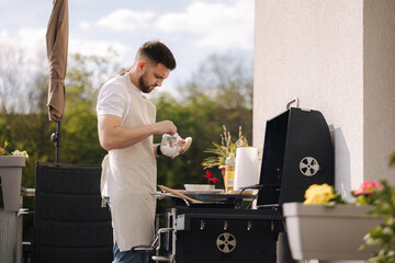 Wall Mural - Man salted food in frying pan and prepare meal outdoor on BBQ grill