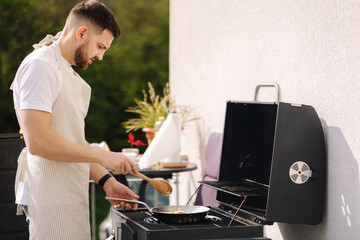 Wall Mural - Handsome man cook outdoor on grill. Man frying some food on frying pan. Summer food on fresh air