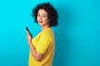 © Roquillo - Rear view photo portrait of Young arab woman wearing yello T-shirt over blue background using smartphone smiling