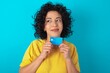 © Roquillo - Photo of cheerful Young arab woman wearing yello T-shirt over blue background hold debit card look empty space