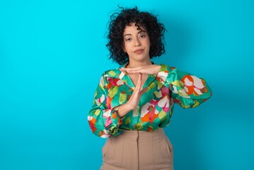 Sticker - young arab woman wearing colorful shirt over blue background being upset showing a timeout gesture, needs stop, asks time for rest after hard work,