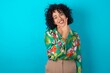 © Jihan - young arab woman wearing colorful shirt over blue background looking confident at the camera smiling with crossed arms and hand raised on chin. Thinking positive.