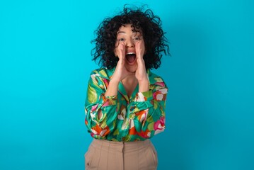 Sticker - young arab woman wearing colorful shirt over blue background shouting excited to front.