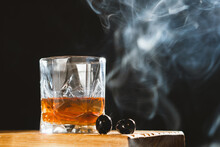 Glass Of Whiskey Rum With Ice Cubes And Black Olives On Wooden Board On Black Backgrand With Smoke