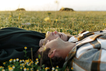 Side view of relaxed young couple lying together on green grass with eyes closed. Relationships concept