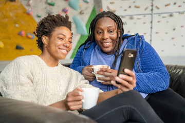 Wall Mural - Mother and daughter looking at smart phone after training on climbing wall