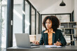 © Nuttapong punna - Confident business expert attractive smiling young woman typing laptop ang holding digital tablet on desk in office.