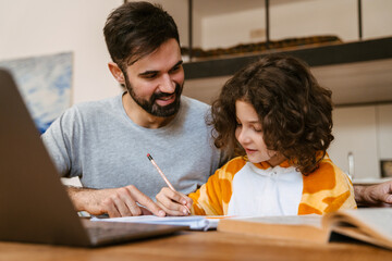 Father helping his son with homework while sitting with laptop at table