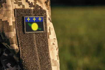 Wall Mural - Close up millitary woman or man shoulder arm sleeve with Guadeloupe flag patch. Troops army, soldier camouflage uniform. Armed Forces, empty copy space for text
