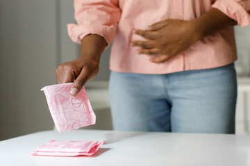 Classic comfort of menstrual pads. Black woman taking sanitary napkin from table, suffering from menstrual pain