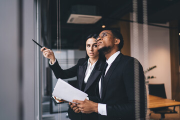 Wall Mural - Thoughtful black businessman with documents standing with female colleague in office