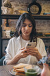 © Tatyana - Portrait of a dark-haired young woman using a smartphone in a cafe.Remote work,business, freelance,blogging,social media concept.
