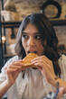 © Tatyana - Portrait of a young attractive dark-haired woman eating a sandwich in a cafe.
