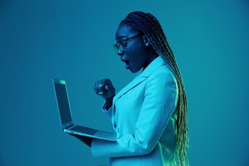 Wall Mural - African African woman with laptop in glasses on a blue background in neon light, color mixed light. Data storage cyber security, hacker, big data.