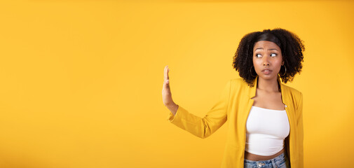 serious african american lady doing stop gesture with hand and looking aside at free space, yellow b