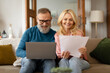 © Prostock-studio - Happy Mature Couple Doing Paperwork And Using Laptop At Home
