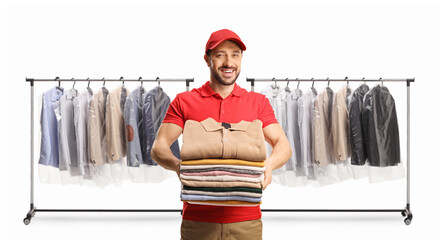 Canvas Print - Male worker holding a pile of folded clothes in front of clothing racks