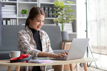 Attractive Asian female freelancer planning her project, working on her tasks on laptop computer at a coffee table in her living room.