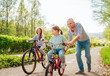 © Soloviova Liudmyla - Smiling father with two daughters during outdoor walk. He teaching younger girl to ride a bicycle. They enjoy togetherness in the summer city park. Happy childhood concept image.