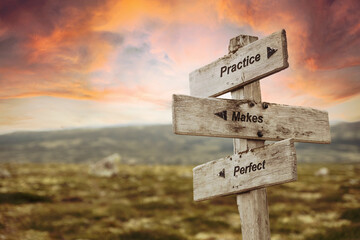practice makes perfect text quote on wooden signpost outdoors in nature. Pink dramatic skies in the background.